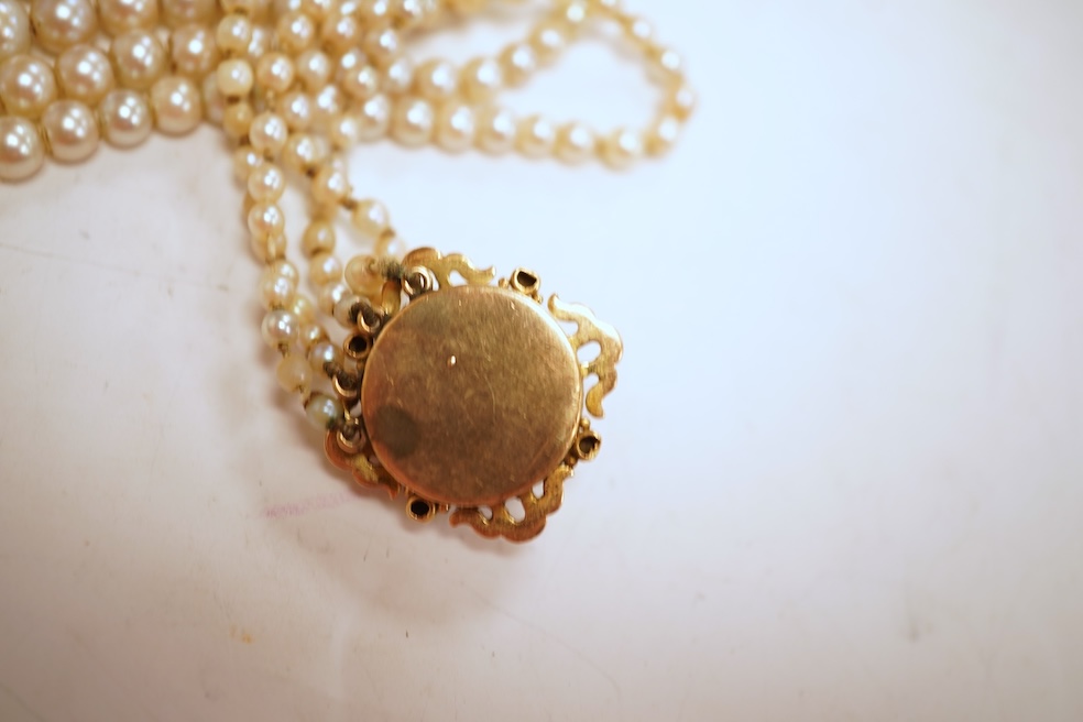 Two necklaces, comprising: a three-strand cultured pearl necklace, to a cabochon garnet and diamond clasp, length 34cm; and a paste and gilt metal pendant on a gold chain, chain length 44cm, stamped 14K, gross weight of